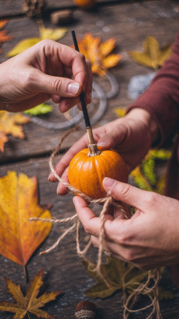A person's hands crafting a DIY fall wall hanging, showcasing a cheap autumn decor idea on a budget.