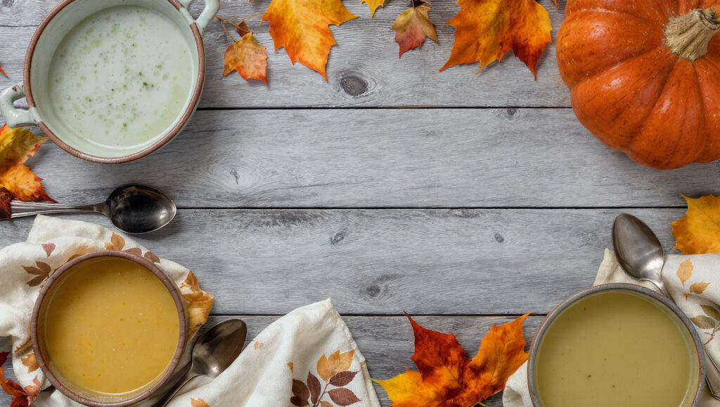 A collection of rustic ceramic soup bowls and wooden spoons on a table, ready for serving delicious autumn soups.